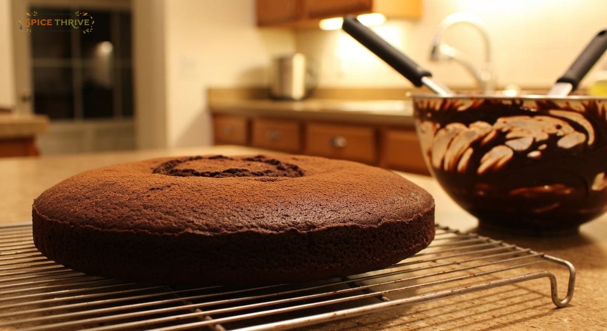 A close-up, in-process photo in a warmly lit home kitchen showing a moist, dark chocolate cake cooli